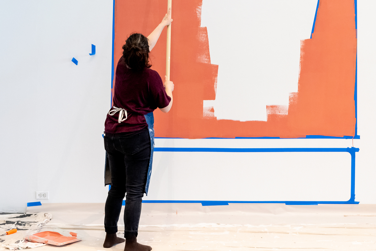 A young woman using a paint roller with taped out sections of color on the wall