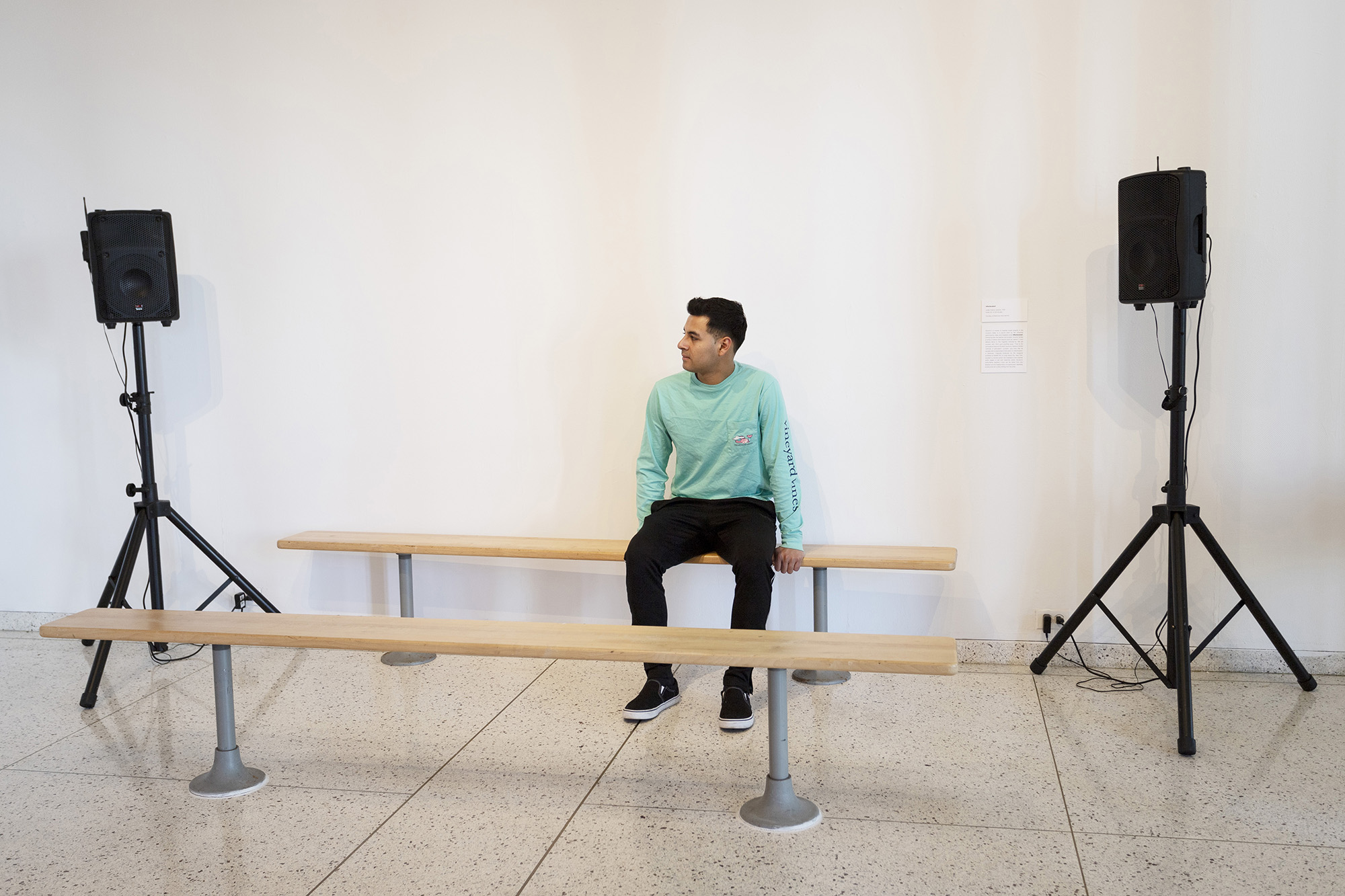 A student sitting on a bench in-between two speakers on stands on either side