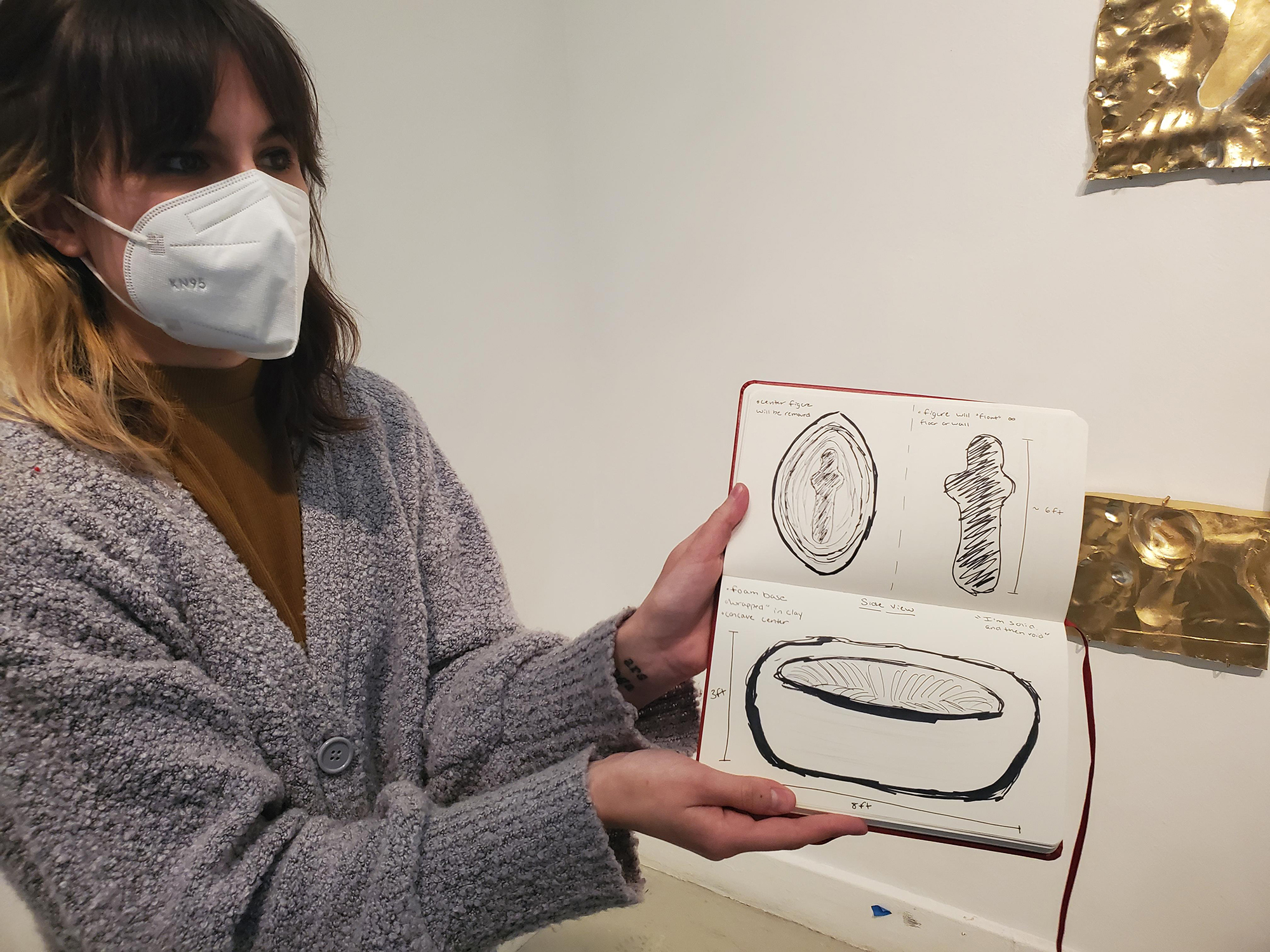 Artist with a N95 mask showing a drawing in their sketchbook.