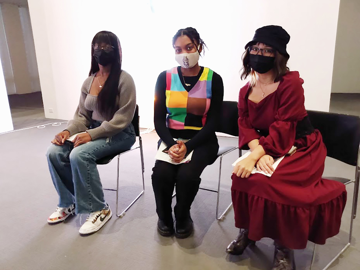 Three students sitting and smiling for the camera under their masks.