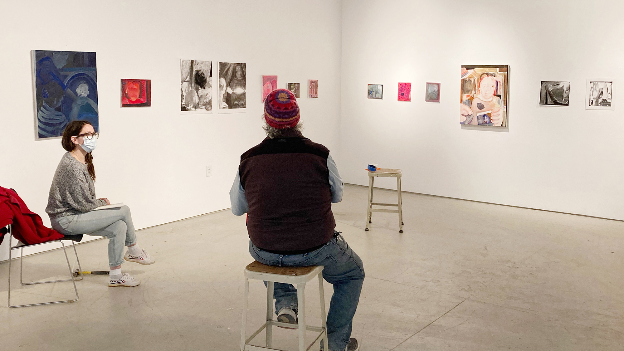 Two people sitting in an art studio in front of paintings and works on paper.